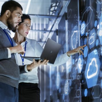 Male IT Specialist Holds Laptop and Discusses Work with Female Server Technician. They're Standing in Data Center, Rack Server Cabinet with Cloud Server Icon and Visualization.