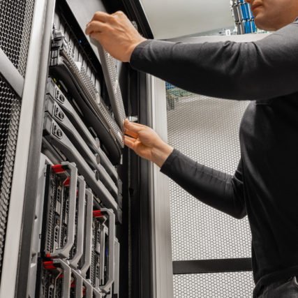 Midsection of male IT technician installing drive in rack at datacenter